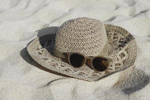 chapeau de paille et lunettes de soleil sur la plage de sable blanc photo