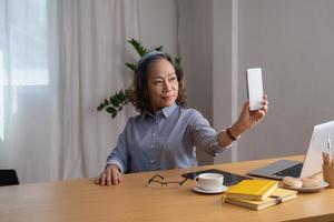 portrait d'une femme âgée tenant un téléphone portable pour prendre une photo d'elle-même pour référence future.