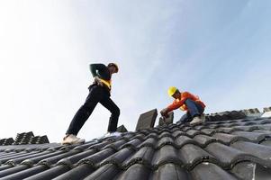 les constructeurs en vêtements de travail installent de nouveaux outils de toiture, des outils de toiture, une perceuse électrique et les utilisent sur de nouveaux toits en bois avec des tôles photo