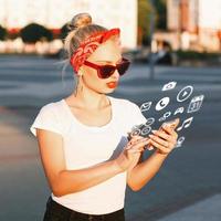 belle fille hipster avec des lunettes de soleil tenant un téléphone avec des icônes volantes. photo