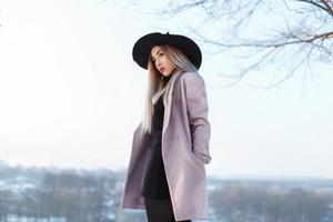jeune fille élégante dans un chapeau et un manteau se dresse sur une colline sur fond de paysage d'hiver photo