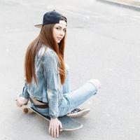 jeune fille élégante dans une veste en jean et un jean assis sur une planche à roulettes. photo