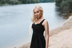 portrait d'une belle femme en robe noire sur la plage au bord de la rivière photo