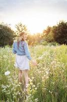 belle fille marchant sur le terrain en été avec des fleurs sauvages. photo