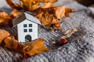 fond automnal. maison de jouets et feuilles d'érable d'automne orange séchées sur un pull en tricot gris. espace de copie de la bannière de thanksgiving. concept de temps froid d'humeur hygge. bonjour l'automne en famille photo