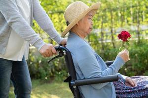 fille soignante embrasse et aide une vieille dame asiatique âgée ou âgée tenant une rose rouge sur un fauteuil roulant dans le parc. photo