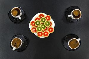 quatre tasses de café du matin et une assiette de biscuits colorés sur une table en bois noire. vue de dessus photo