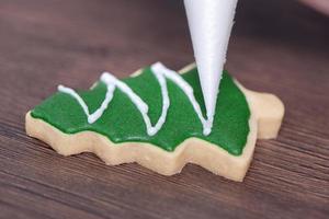 gros plan sur le dessin d'un biscuit au sucre d'arbre de noël sur fond de table en bois avec glaçage. photo