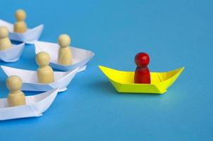 concept de leadership - figure en bois rouge sur origami de bateau en papier jaune menant le reste de la figure sur un bateau en papier blanc. photo