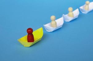 concept de leadership - figure en bois rouge sur origami de bateau en papier jaune menant le reste de la figure sur un bateau en papier blanc. photo