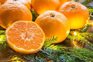 mandarines fraîches dans des lumières de guirlande, sur des branches de sapin et des guirlandes - fond lumineux du nouvel an. la moitié d'une orange, arôme d'agrumes de la fête. noël, nouvel an. espace pour le texte. photo