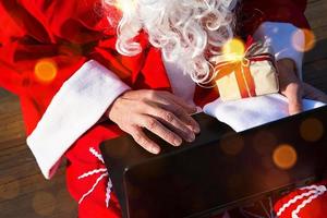 le père noël avec un ordinateur portable et un cadeau à la main. commandez des cadeaux pour Noël et le nouvel an via la boutique en ligne. réserver les services d'un animateur pour les vacances. photo