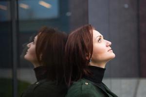 une femme brune avec une coupe de cheveux bob se tient dos au mur en miroir, se reflète et a l'air triste. le thème de la solitude photo