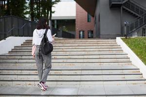 une étudiante avec un sac à dos noir et un cahier dans les mains se tient sur les marches devant l'institut. l'enseignement supérieur, la rentrée, la rentrée. fond photo