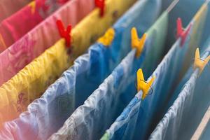 le linge de lit et les serviettes colorés et propres après le lavage sont suspendus aux barres de la sécheuse et fixés avec des pinces à linge jaunes et rouges. nettoyage général, séchage du linge, sèche-linge compact pour la maison. photo