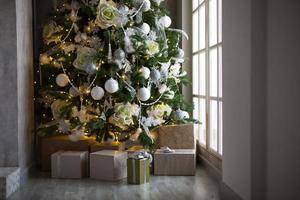 coffret cadeau dans un emballage doré et un arc argenté sous le sapin de noël avec un décor blanc. nouvel an, réveillon de noël, salutations pour la famille, réconfort et attente d'un miracle photo