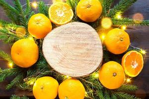 fond de vacances du nouvel an sur une coupe ronde d'arbre entouré de mandarines, de branches de sapin vivantes et de guirlandes de lumières dorées, avec un espace en bois pour le texte. arôme d'agrumes, tranches d'orange, noël. Cadre photo