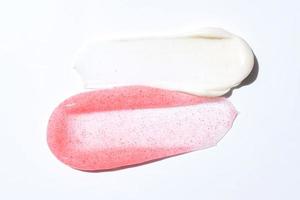 crème et gommage coups de frottis isolés sur fond blanc. texture de gommage exfoliant cosmétique. échantillons de masque de soin rose et blanc photo