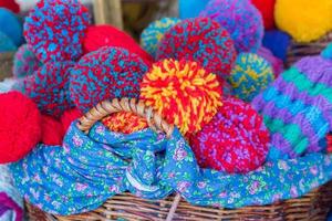 un panier tressé rempli de bonnets tricotés aux couleurs vives avec de gros pompons photo