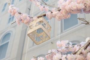 cage à oiseaux décorative blanche accrochée à une branche de pommier en fleurs sur fond de construction. décoration de la ville de printemps photo