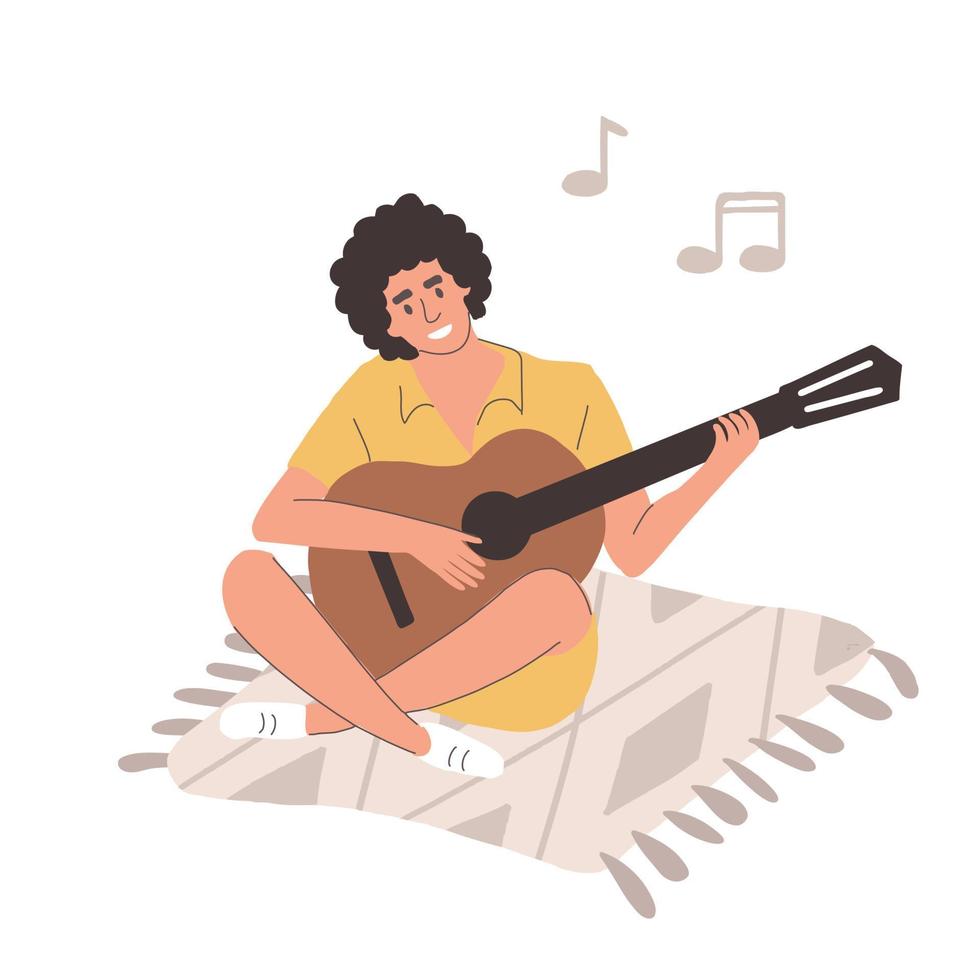 un jeune homme est assis sur une couverture et joue de la guitare. le gars sourit chante des chansons et pince les cordes avec ses jambes repliées sur un fond blanc vecteur
