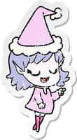 dessin animé autocollant en détresse heureux d'une fille elfe pointant portant un bonnet de noel vecteur