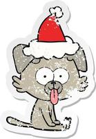 dessin animé autocollant en détresse d'un chien assis avec la langue qui sort portant un bonnet de noel vecteur