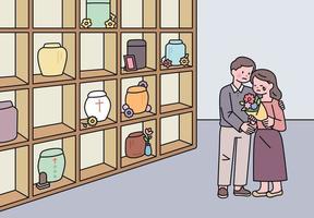 un homme et une femme pleurent avec des fleurs dans une maison commémorative avec une urne de crémation.