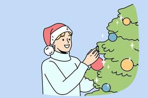 jeune homme souriant en bonnet de noel décorer le sapin de noël avec des boules colorées. un gars heureux s'amuse avec une décoration de sapin à la maison pour célébrer le nouvel an. illustration vectorielle. vecteur