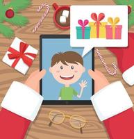 le père noël tient une tablette et discute avec un jeune enfant qui parle de cadeaux qu'il aimerait recevoir à noël vecteur