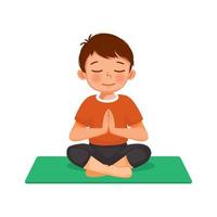 mignon petit garçon faisant des exercices de fitness gymnastique pratiquant la méditation de yoga assis dans la pose de lotus sur un tapis vert à l'intérieur à la maison