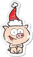 joyeux cochon assis autocollant en détresse dessin animé d'un bonnet de noel vecteur