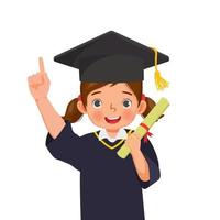 jolie petite écolière en chapeau de graduation et robe tenant un certificat de diplôme pointant le doigt vers le haut vecteur