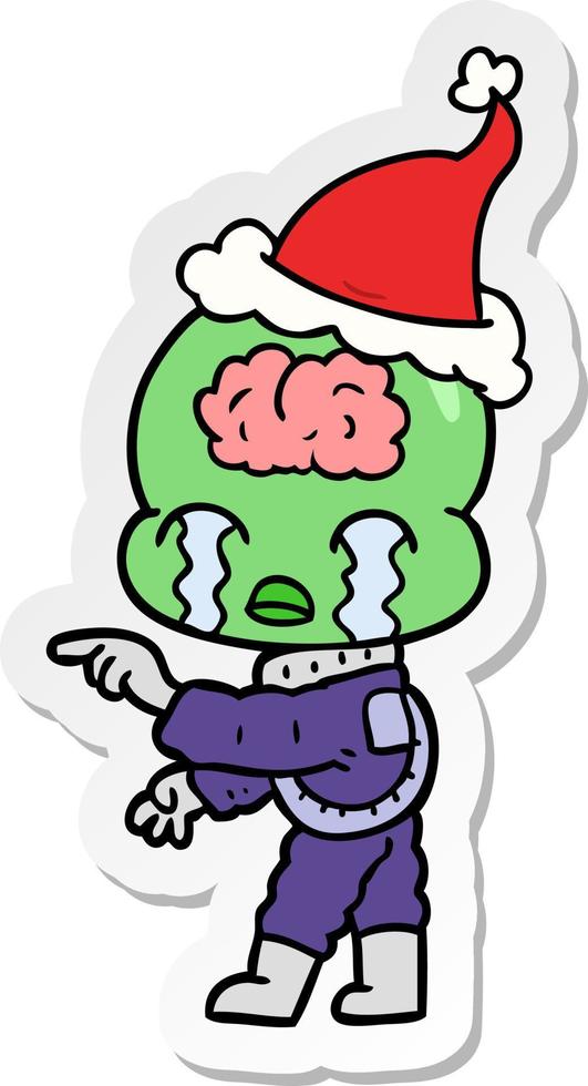 desenho de adesivo de um alienígena de cérebro grande chorando e apontando usando chapéu de papai noel vetor