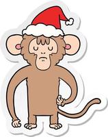 desenho de adesivo de um macaco coçando usando chapéu de papai noel vetor