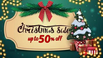 promoção de natal, desconto de até 50, banner de desconto verde com moldura vintage, galhos de árvore de natal com laço vermelho, guirlanda e árvore de natal em um pote com presentes vetor