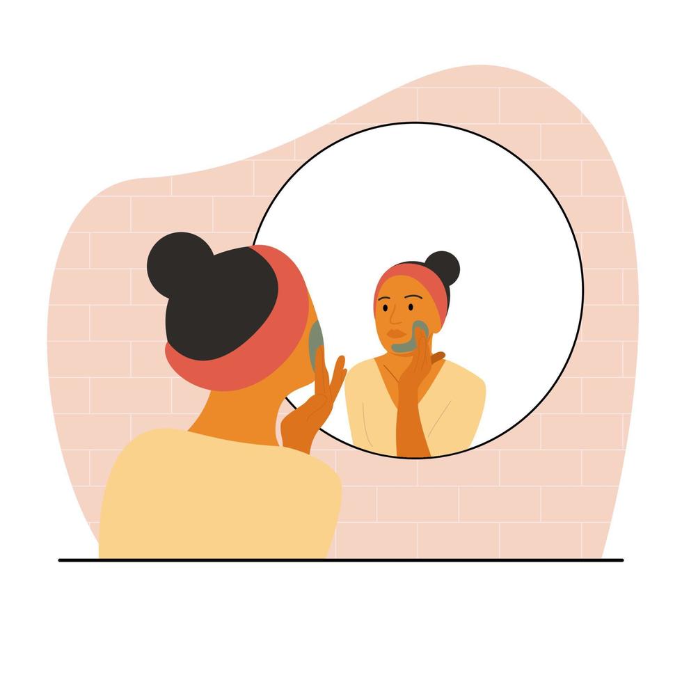 una donna dalla pelle marrone si siede davanti a uno specchio e si applica una maschera sul viso. routine cosmetica domestica prima di andare a letto. una donna con una benda sulla testa. vettore