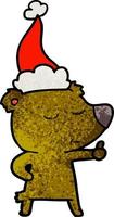 felice cartone animato strutturato di un orso che dà i pollici in su indossando il cappello di Babbo Natale vettore