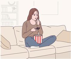 una donna è seduta sul divano e mangia popcorn e guarda un film. vettore