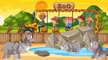 zoo al tramonto con molti bambini che guardano il gruppo di rinoceronti vettore