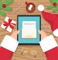 babbo natale è seduto alla sua scrivania sul posto di lavoro e riceve una lettera sul suo tablet - illustrazione vettoriale di design piatto