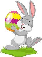 piccolo coniglio del fumetto che tiene l'uovo di Pasqua nell'erba vettore