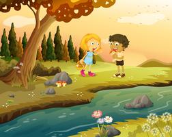 Un ragazzo e una ragazza che giocano nella foresta vicino alla riva del fiume vettore