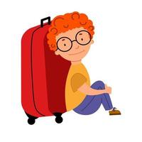 un simpatico ragazzo dai capelli ricci dai capelli rossi con gli occhiali è seduto accanto a una valigia. vettore
