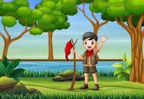 un boy scout con in mano una bandiera che cammina nella foresta vettore