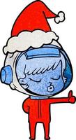 cartone animato testurizzato di una bella ragazza astronauta che dà i pollici in su indossando il cappello di Babbo Natale vettore